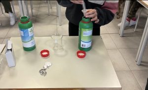 Una studentessa o uno studente preleva con una siringa del liquido da una bottiglia verde.