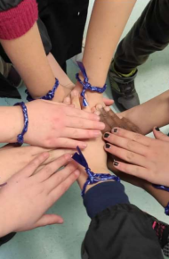 Mani di studentesse e studenti sono unite al centro, portano tutte un braccialetto blu