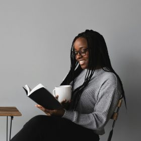 Una ragazza sorride mentre legge un libro tenendo una tazza