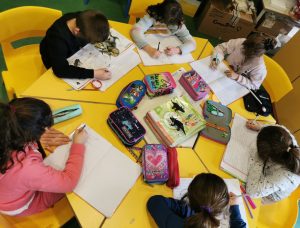 Delle bambine scrivono sui loro quaderni. Sul tavolo sono presenti libri sui dinosauri.