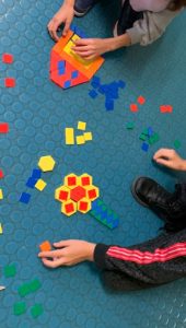 Bambine e bambini formano figure come fiori, casette e omini componendo mosaici con quadratini e triangolini di plastica
