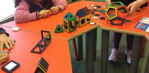 Bambine e bambini studiano figure geometriche tridimensionali incastrando assieme pezzi di plastica di forme diverse