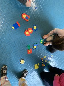 Bambine e bambini formano figure come fiori, casette e omini componendo mosaici con quadratini e triangolini di plastica